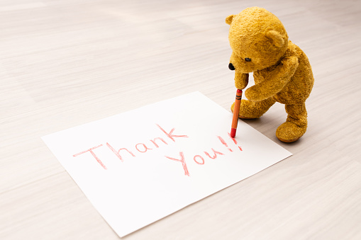 Teddy bear writing thank you with crayon on paper