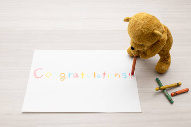 Teddy bear writing congratulations on paper with crayons