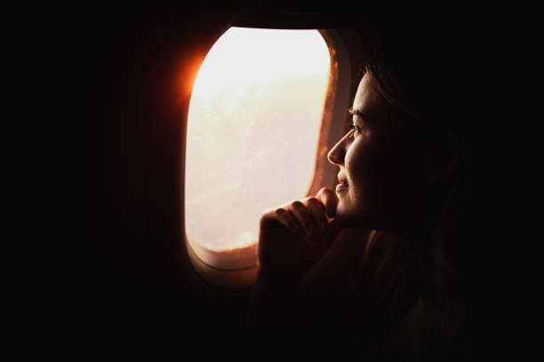 Smiling woman day dreaming while looking through an airplane window at sunset.