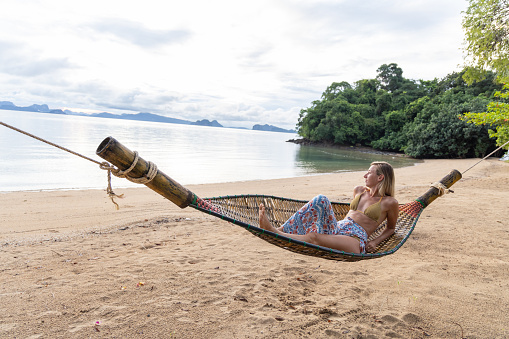 30's woman relaxing on hammock over sea in Thailand, Southeast Asia vacations.