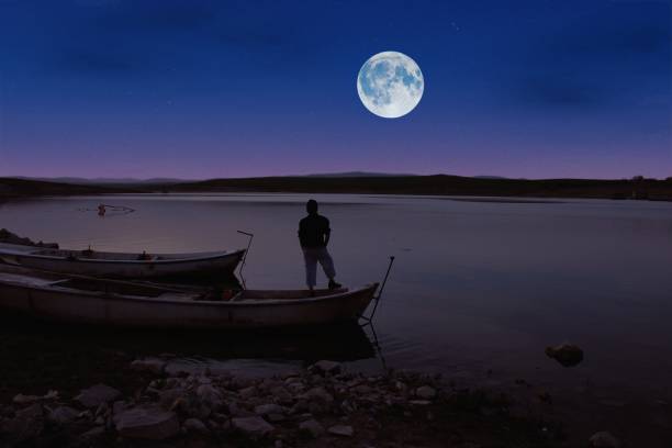 istock Man watching the full moon from the boat by the lake. 1450660555