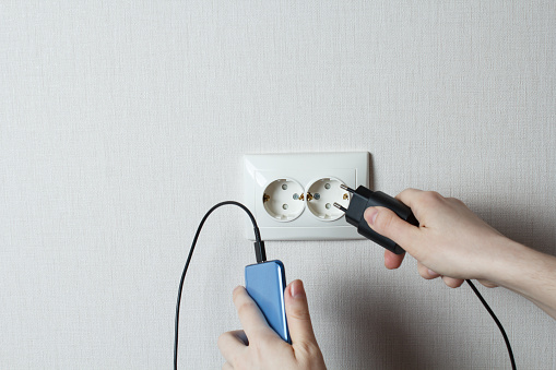 the girl connects the mobile phone to the socket.