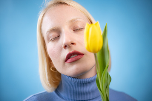 Portrait of a carefree blond woman with yellow tulip against blue background.
