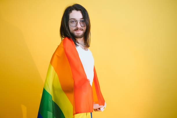 uomo gay tenere bandiera a strisce arcobaleno isolato sul ritratto di studio sfondo colorato. persone lifestyle moda concetto lgbtq - twink foto e immagini stock