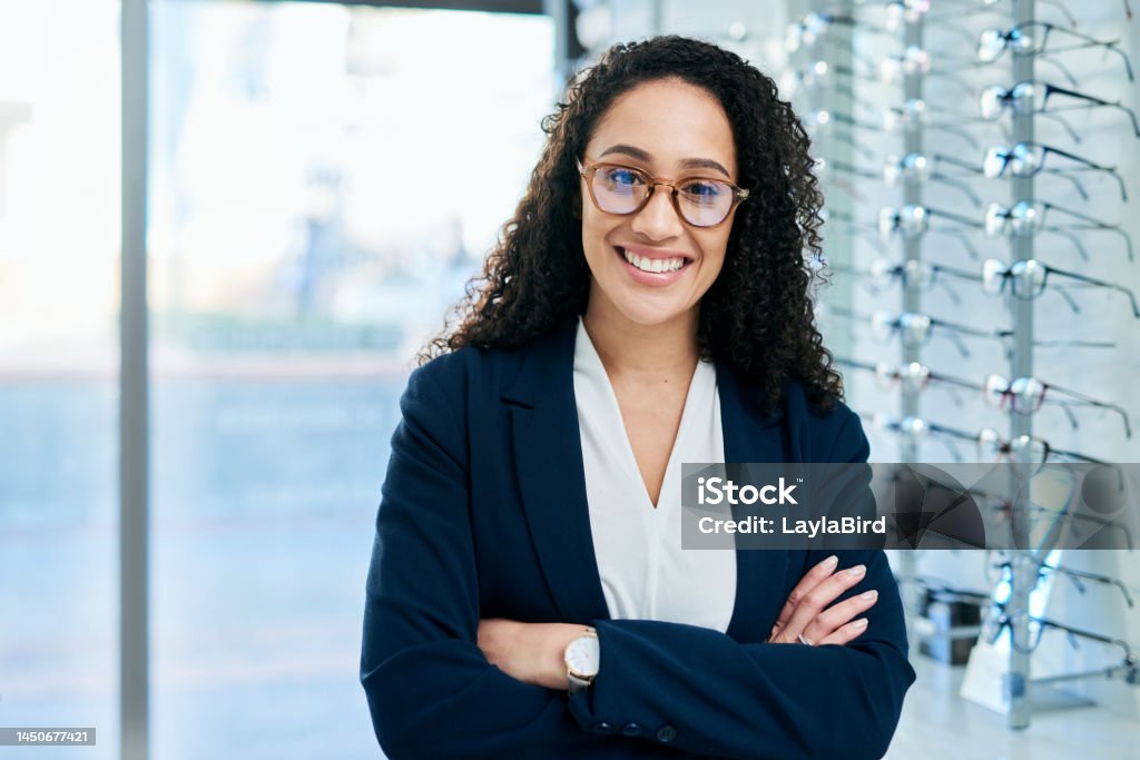Optometrist, portrait and woman, arms crossed and optician, eye care service and consulting prescription lenses, glasses and frame in store. Happy ophthalmologist, professional clinic and vision shop Portrait Stock Photo
