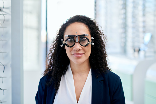 Optometrist store, woman smile and phoropter for eye test, vision or visual healthcare. Happy black woman, medical lens device or eye health for customer, client or consumer in portrait at optician