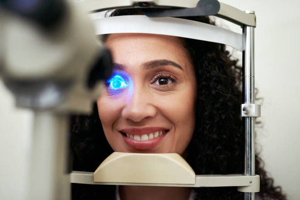 istock Eye vision and test machine light for scan, optometrist and professional consulting check up. Wellness, patient and consultation for eye exam of black woman at slit lamp with focused smile. 1450677569