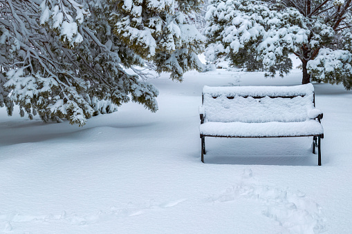 A park bench is covered with freshly fallen snow after a winter snowstorm.