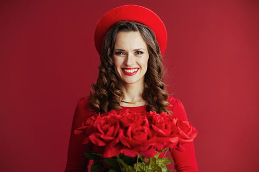 Happy Valentine. smiling modern middle aged woman in red dress and beret isolated on red background with red roses.