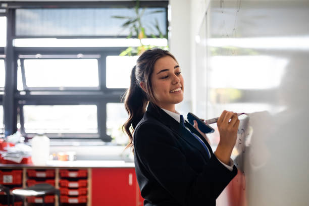 Happy to be Learning A side-view shot of a female student in a classroom at a school. She is wearing a school uniform and writing on notes on a whiteboard. polyethylene molecular structure stock pictures, royalty-free photos & images