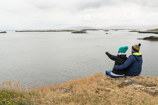 Couple sitting at the edge of a cliff and pointing out the horizon in breiðafjörður, Iceland.