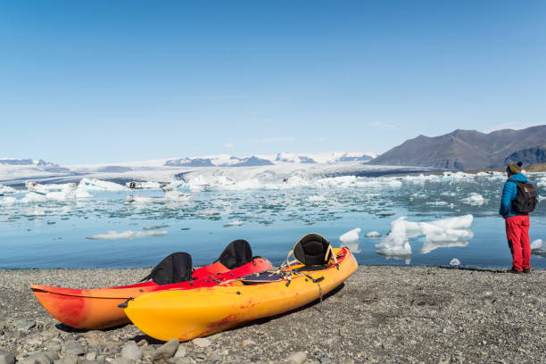 Young man close to two kayaks at a lakeshore of a Jökulsárlón glacier lagoon in Iceland. Young man close to two kayaks at a lakeshore of a Jökusárlón glacier lagoon in Iceland. jokulsarlon stock pictures, royalty-free photos & images