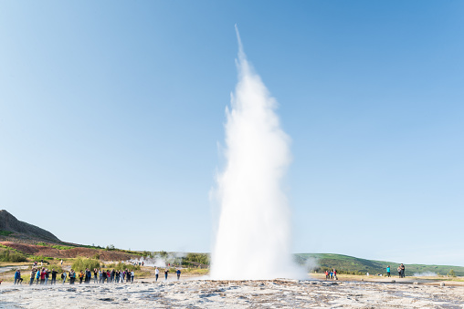 A group of people looking at an icelandic geyser erupting.