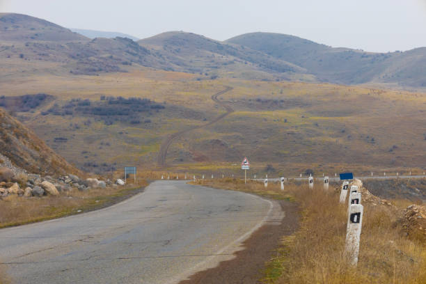 A bent asphalt road against the backdrop of a curved dirt path going up the hill