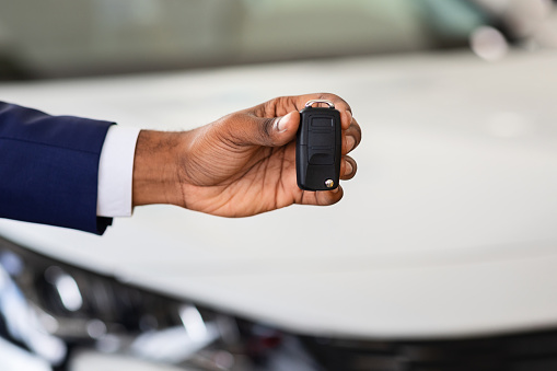 Auto Sale Concept. Closeup Of Car Keys In African American Man Hand, Unrecognizable Black Male Dealership Center Manager In Suit Holding Automobile Key Over Luxury Vehicle On Background, Cropped