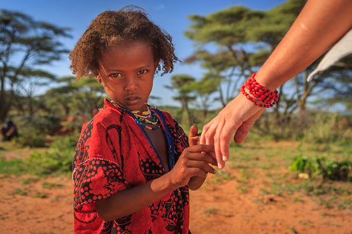 Young caucasian female volunteer holding hand of african child's hand in Ethiopian village.