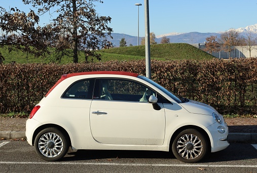 Udine, Italy. December 18, 2022. White and red convertible Fiat 500 C Cabrio. Side view , public park on background
