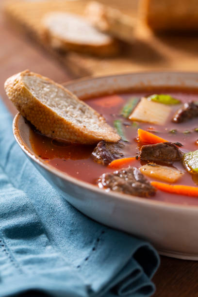Bowl of fresh hot beef vegetable soup with green beans, potato, carrrots, and celery with rustic bread.