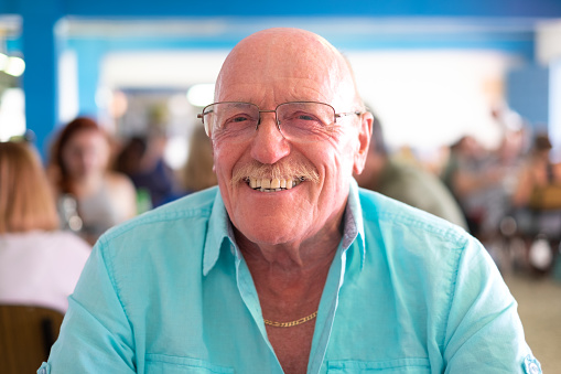Portrait of attractive happy senior man sitting at a restaurant table looking at camera. Elderly smiling grandfather enjoying relaxed lifestyle during retirement