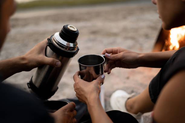 ein paar reisende trinken kaffee. herbstpicknick am sea beach. mann gießt kaffee aus thermoskanne. frau hält metallbecher mit getränk. lifestyle-moment in der natur. aufschließen. - getränkebehälter mit isolierung stock-fotos und bilder