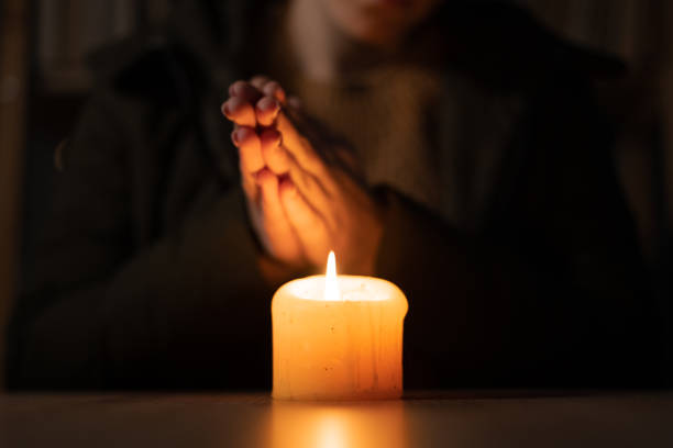 istock Close up womans hands dressed in a warm winter jacket sit at home at a table and warms his hands from a burning candle. no heating and electricity in winter at home. 1450712440