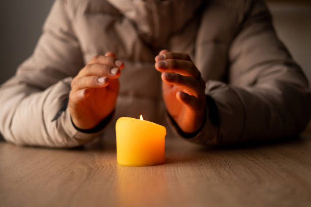 istock A man dressed in a warm winter jacket sits at home at a table and warms his hands from a burning candle, close up. no heating in winter at home. 1450712480