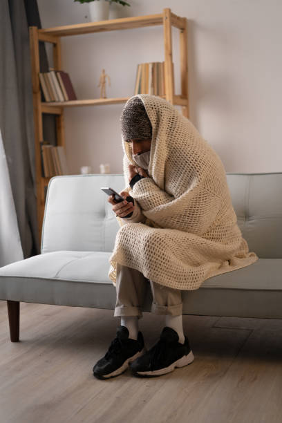 istock Young man dressed in winter clothes feeling cold sitting at home with no heating, gaming on smartphone. No heating 1450712507