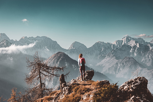 Scenic mountain view and one lonely woman hiker standing at a view point looking at the Alps