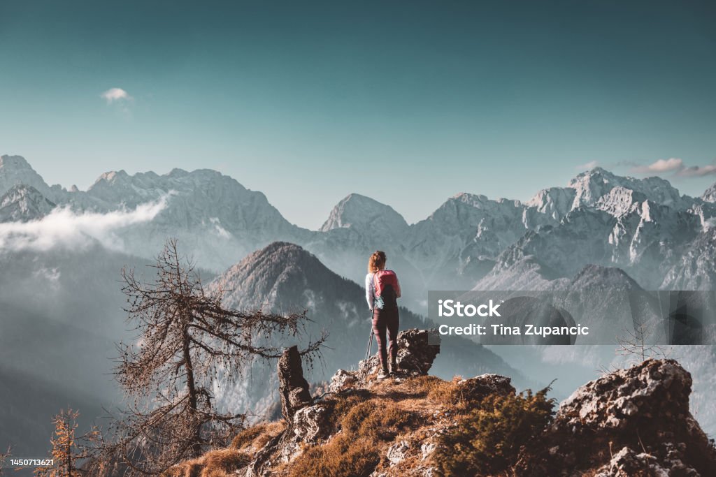 Scenic mountain view and one lonely woman hiker standing at a view point looking at the Alps Scenic view of autumn mountain, European Alps, from a view point, where caucasian woman hiker is standing. Sun is shining high up in the mountains, a light mist in the valleys down bellow. Woman mountaineer enjoying the view of majestic Alps on a sunny autumn day. Mountain Stock Photo Scenic mountain view and one lonely woman hiker standing at a view point looking at the Alps Scenic view of autumn mountain, European Alps, from a view point, where caucasian woman hiker is standing. Sun is shining high up in the mountains, a light mist in the valleys down bellow. Woman mountaineer enjoying the view of majestic Alps on a sunny autumn day. Mountain Stock Photo