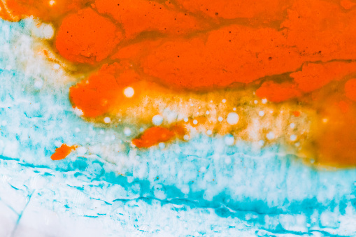 Macro close up depicting the abstract forms and shapes in a mixture of blue and orange paint and oil.