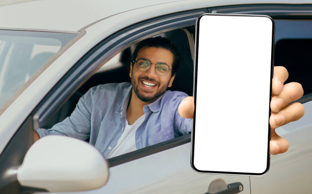 istock Happy Young Indian Man Showing Big Blank Smartphone While Sitting In Car 1450715190