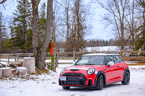 Toronto, Ontario, Canada- December 17, 2022. Chili red colour MINI COOPER at the rural location in Southern Ontario, Canada. This is a popular local meet of Cars & Coffee where various car enthusiasts get together. This is the third generation model F56 JCW, since BMW took over iconic brand of MINI. MINI featured in the photo is John Cooper Works model, the most powerful 2 door version. For the first time, this compact car features engine build and designed by BMW, and packs even more power and torque than previous models since 2002 to present. Original design clues and themes are still present on this brand new model. Mini has been around since 1959 and has been owned and issued by various car manufacturers.