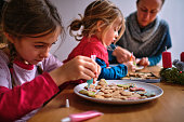 Mother and two daughters decorating homemade gingerbread cookies before Christmas.