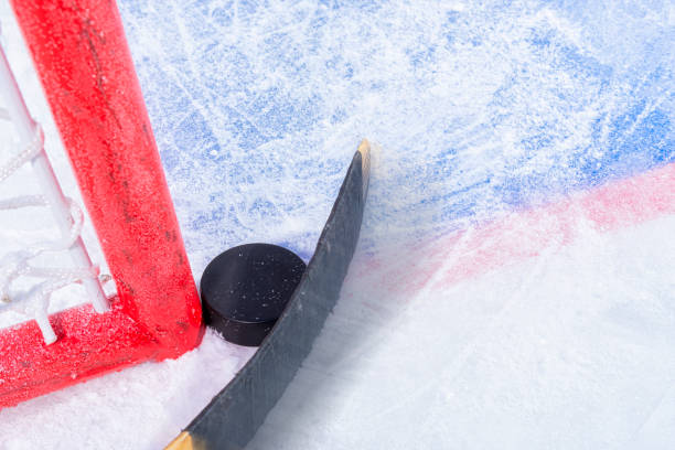 Attempting to score a goal in ice hockey, with the puck stuck between the goal post and the goal with a hockey stick in motion.