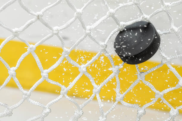 primer plano de un disco de hockey sobre hielo golpeando la parte posterior de la red mientras las virutas de hielo vuelan - ice hockey hockey puck playing shooting at goal fotografías e imágenes de stock