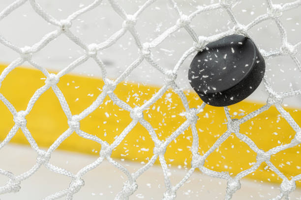 Close-up of an Ice Hockey puck hitting the back of the net as ice shavings flies stock photo