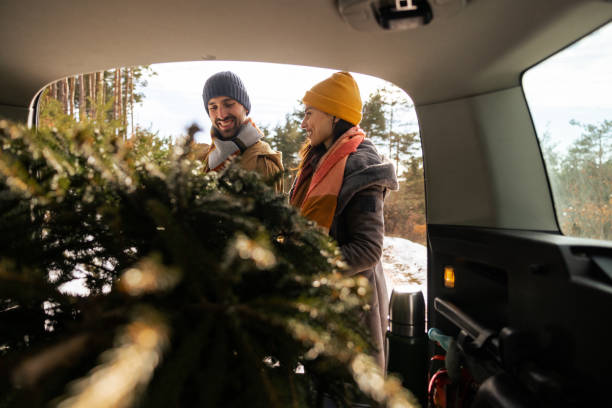 istock Young couple packing a Christmas tree into car trunk 1450724530