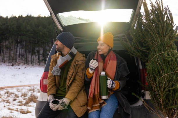 istock Young couple sitting in a car trunk, drinking tea while resting after Christmas tree search 1450727001
