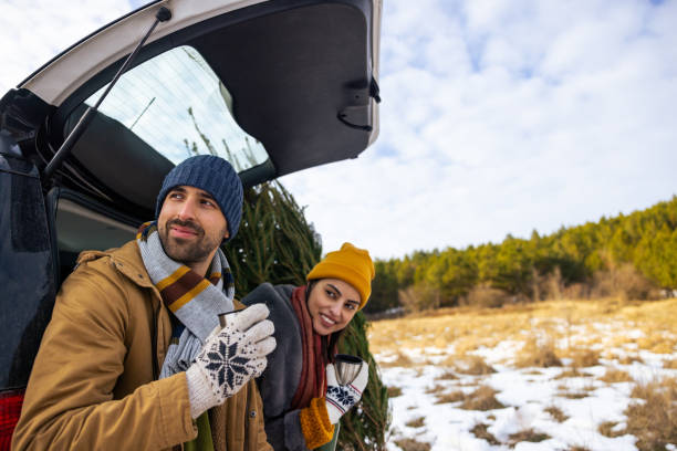 istock Couple sitting in a car trunk, drinking tea and looking at view, while resting after Christmas tree search 1450727667