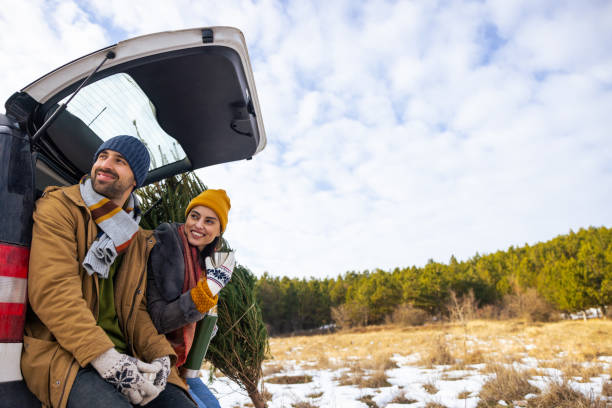 istock Couple sitting in a car trunk, drinking tea and looking at view, while resting after Christmas tree search 1450727739