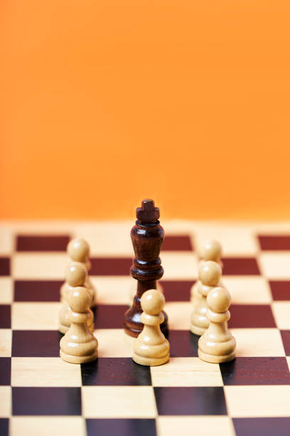 Chess group of white pawns with black king challenge center on orange background stock photo