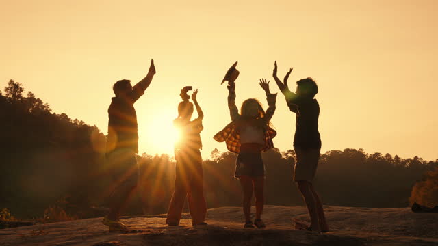 Silhouette of group of friends throwing their hats and high five as celebration for reaching the mountain peak