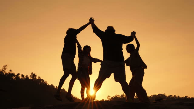 Silhouette of group of friends having fun by spinning and dancing in a circle