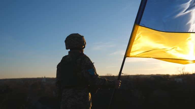 Soldier of ukrainian army holding waving flag of Ukraine against background sunset. Man in military uniform and helmet lifted up flag. Victory against russian aggression. Invasion resistance concept