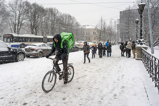 Riga, Latvia - November 26, 2022. Courier of Bolt company rides with bicycle, during snowfall in Riga city.
