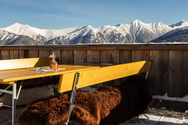 tisch und bänke mit fellen in einem bergcafé mit blick auf die schneebedeckten alpenberge, österreich, salzburg - apres ski ski restaurant mountain stock-fotos und bilder