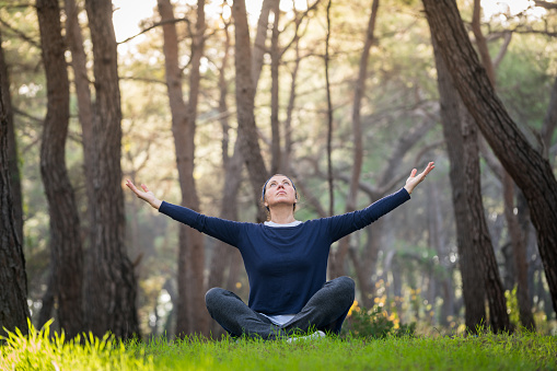 Mature woman practicing yoga workout routine in wood forest.