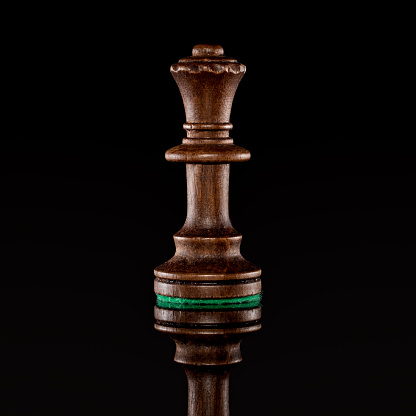 Wooden black chess queen isolated at dark background with transparent reflection on the floor