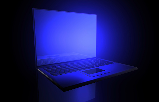 Laptop under blue light glows from its screen in the dark.