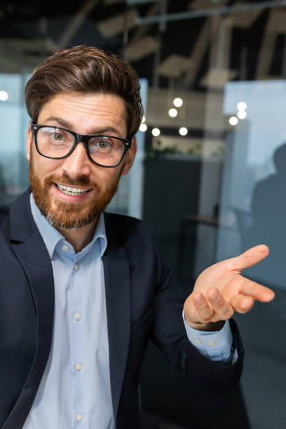 plan vertical, un homme d’affaires au bureau parle à des collègues et amis à l’aide d’une application sur un smartphone, un homme mûr en costume d’affaires à l’intérieur du bureau sourit amicalement - working smiling equipment car photos et images de collection